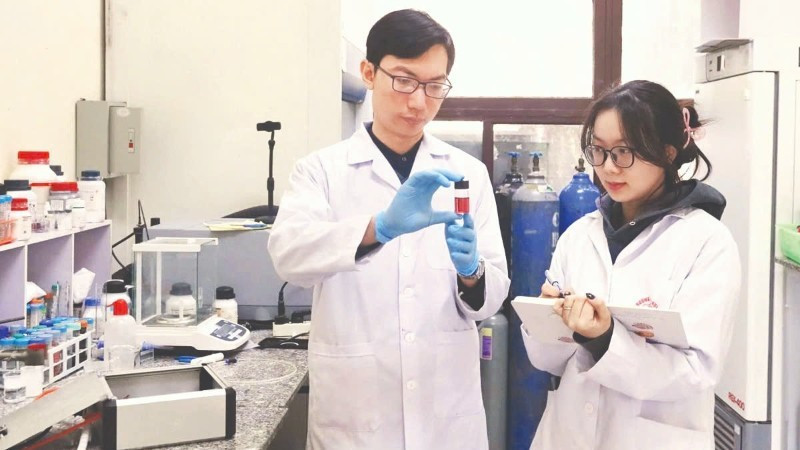 Tiến sĩ Nguyễn Nhật Linh hướng dẫn sinh viên kiểm tra mẫu sản phẩm hạt nano vàng thu được từ quá trình tổng hợp plasma. Ảnh: MINH ĐỨC