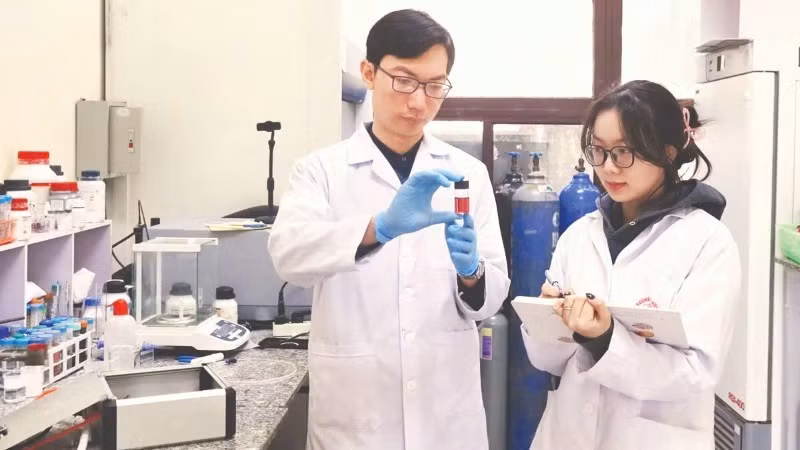 Tiến sĩ Nguyễn Nhật Linh hướng dẫn sinh viên kiểm tra mẫu sản phẩm hạt nano vàng thu được từ quá trình tổng hợp plasma. Ảnh: MINH ĐỨC