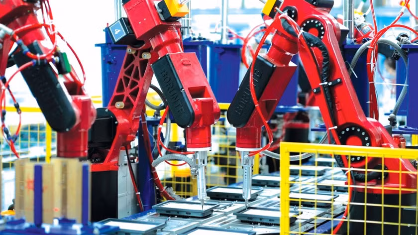 The image shows a highly automated factory floor with several red, robotic arms assembling products.AI-generated content may be incorrect.