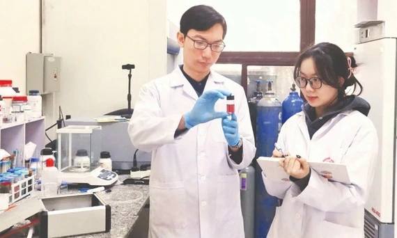 Tiến sĩ Nguyễn Nhật Linh hướng dẫn sinh viên kiểm tra mẫu sản phẩm hạt nano vàng thu được từ quá trình tổng hợp plasma. Ảnh: MINH ĐỨC