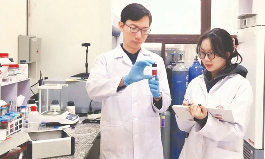 Tiến sĩ Nguyễn Nhật Linh hướng dẫn sinh viên kiểm tra mẫu sản phẩm hạt nano vàng thu được từ quá trình tổng hợp plasma. Ảnh: MINH ĐỨC